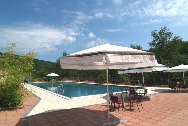 Ein schöner Pool mit Liegestühlen und Sonnenschirmen. Umgeben von grünen Bäumen und einem klaren Himmel.