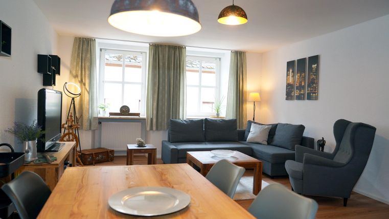 Ein gemütliches Wohnzimmer mit einem modernen Sofa und einem Essbereich. Große Fenster lassen viel Tageslicht herein und verleihen dem Raum eine einladende Atmosphäre.