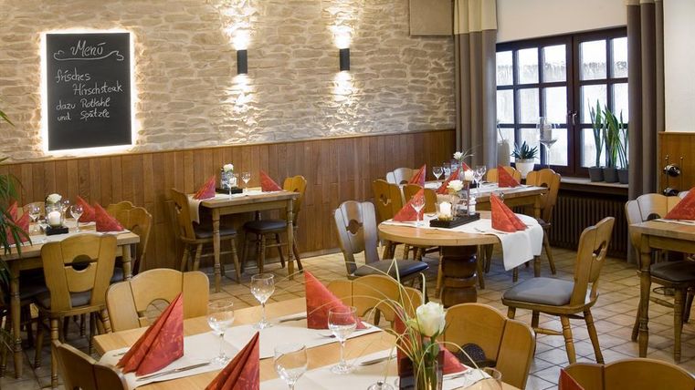 Ein gemütliches Restaurant mit Holzstühlen und Tischen. Die Tische sind mit weißen Tischdecken und roten Servietten dekoriert.