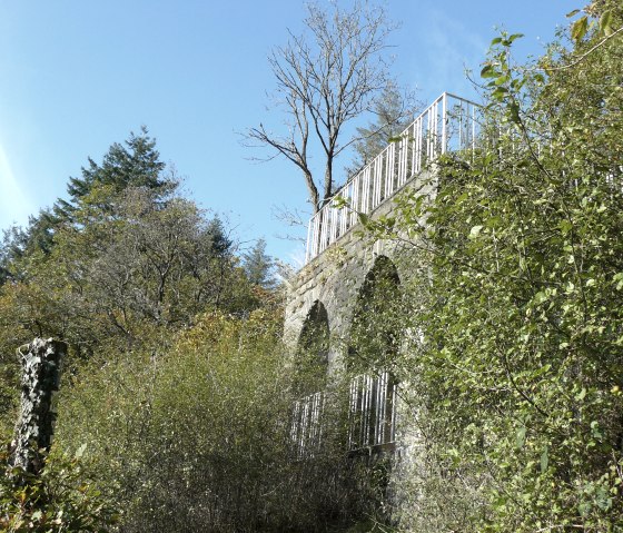Mur de pierre avec balustrade au milieu d'arbres et d'arbustes, ciel bleu en arrière-plan., © Christian Calonec-Rauchfuss, Felsenland Südeifel Tourismus GmbH