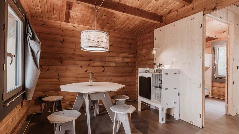 Ein gemütlicher Raum mit Holzverkleidung und einem runden Tisch. Es gibt mehrere Hocker und ein kleines Küchenfeld.