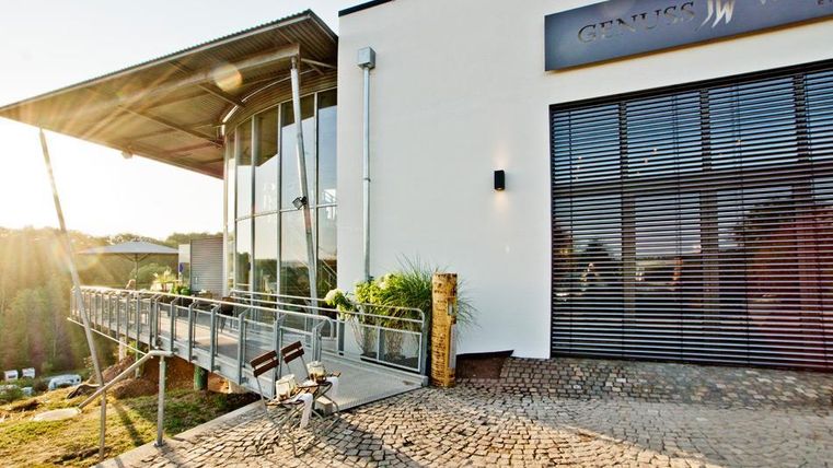 Ein modernes Gebäude mit großen Fenstern und einer Veranda. Im Vordergrund steht ein Fahrrad auf einem gepflasterten Platz.