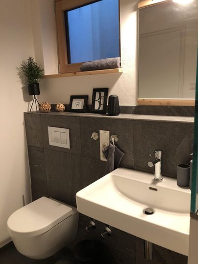 Een moderne badkamer met een grijs betegelde muur en een elegant badkamermeubel. Een grote spiegel en een kleine plantdecoratie zorgen voor een uitnodigende sfeer.