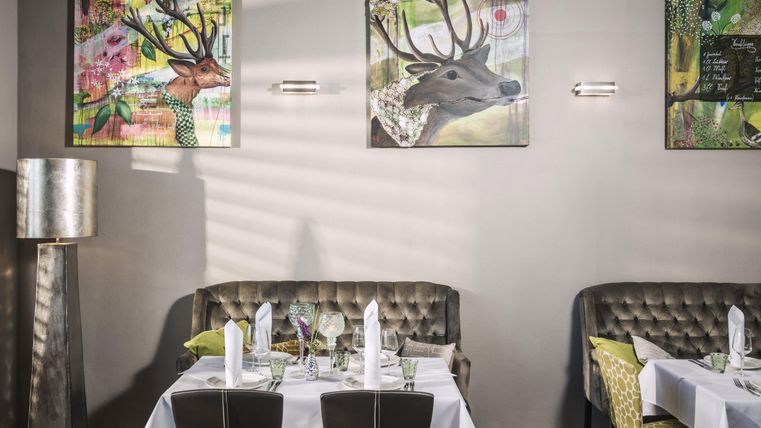 Ein stilvolles Restaurant mit eleganten Tischen und gemütlichen Sitzbänken. Die Wände sind mit bunten Tierporträts dekoriert.