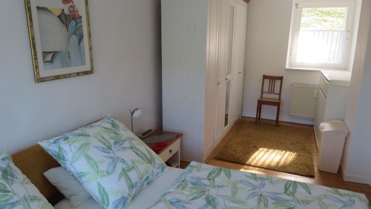 Ein helles Schlafzimmer mit einem Doppelbett und frischem Bettzeug. Es gibt einen Schrank, einen Stuhl und viel Tageslicht.