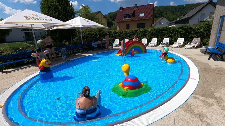 Ein bunter Schwimmbecken mit mehreren aufblasbaren Spielzeugen. Kinder genießen das Wasser an einem sonnigen Tag.