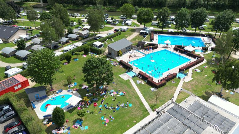 Ein schöner Campingplatz mit mehreren Schwimmingpools und viel Grün. Menschen entspannen sich auf Liegen und der Umgebung.