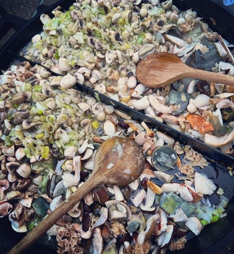 Une grande poêle avec un mélange de fruits de mer frais, de légumes et d'herbes. Deux cuillères en bois sont prêtes à remuer.