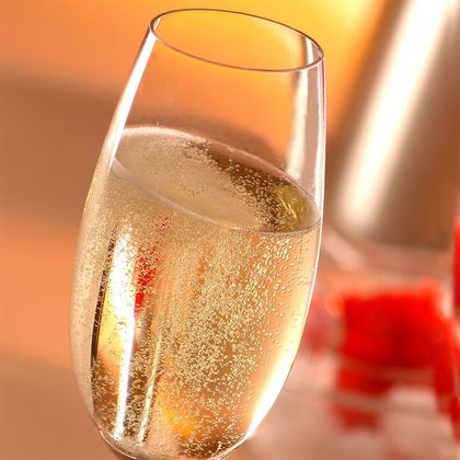 Ein Glas mit sprudelndem Getränk steht vor einem verschwommenen Hintergrund. Es ist elegant und einladend, ideal für festliche Anlässe.