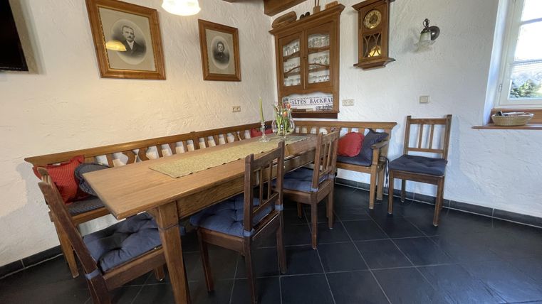 Ein gemütlicher Essbereich mit einem Holztisch und Stühlen. Die Wände sind mit Bildern und einer Uhr dekoriert, und es gibt viel natürliches Licht.