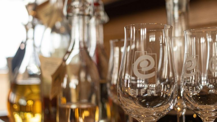 Eine Aufnahme von eleganten Weingläsern und verschiedenen Flaschen mit Getränken. Der Hintergrund zeigt eine stilvolle Präsentation von spirituosenähnlichen Getränken.
