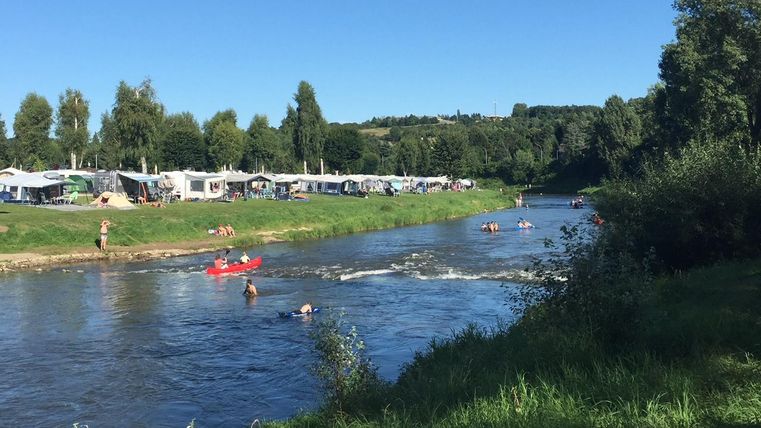 Ein schöner Fluss mit Schwimmern und Kanufahrern. Im Hintergrund sind Campingplätze unter einem klaren blauen Himmel zu sehen.