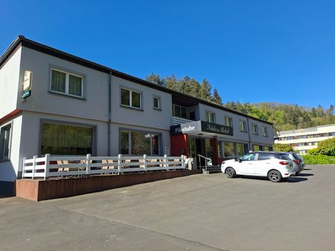 Une petite auberge avec une façade claire et une entrée accueillante. Devant le bâtiment, plusieurs voitures sont garées.