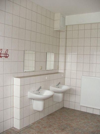 Ein schlichtes Badezimmer mit zwei Waschbecken und großen Wandspiegeln. Die Wände sind gefliest und der Boden ist mit Plattenbelag ausgestattet.