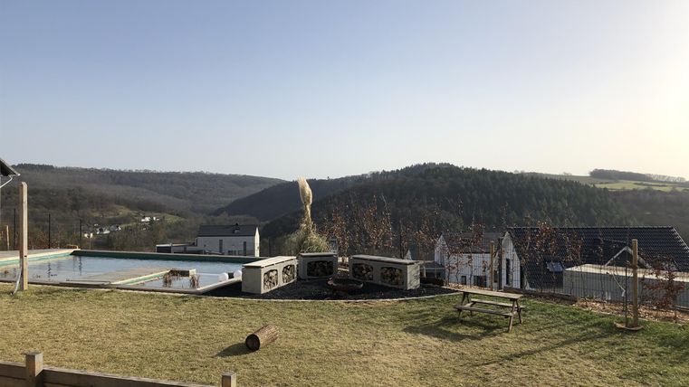 Een rustige uitkijk over zachte heuvels en het dorp in de vallei. Op de voorgrond bevindt zich een verzorgde tuin met banken en speeltoestellen.