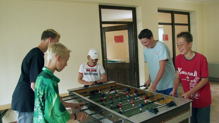 Fünf Jugendliche spielen Tischfußball in einem hellen Raum. Es gibt ein entspanntes und fröhliches Ambiente.