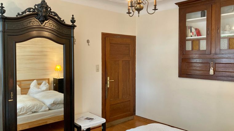 Une chambre confortable avec un grand miroir, une armoire en bois et un lit double. Les murs sont peints dans des couleurs neutres et une lampe fournit une lumière chaude.