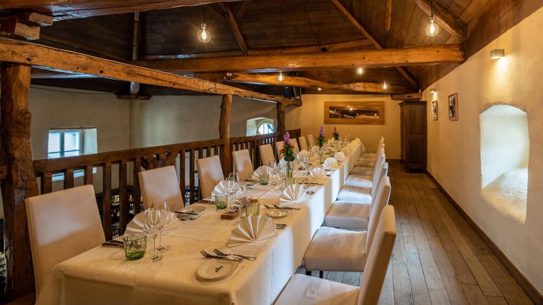 Ein eleganter Essbereich mit langen Tischen und weißen Tischdecken. Die Holzbalkendecke und sanfte Beleuchtung schaffen eine gemütliche Atmosphäre.