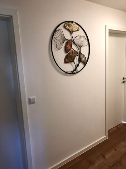 Ein heller Flur mit einem runden Wanddekor aus metallischen Blättern. Rechts ist eine Tür, die in einen weiteren Raum führt.