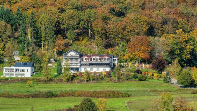 Ein malerisches Hotel umgeben von bunten Herbstbäumen. Die grüne Wiesenlandschaft bietet eine ruhige und idyllische Atmosphäre.