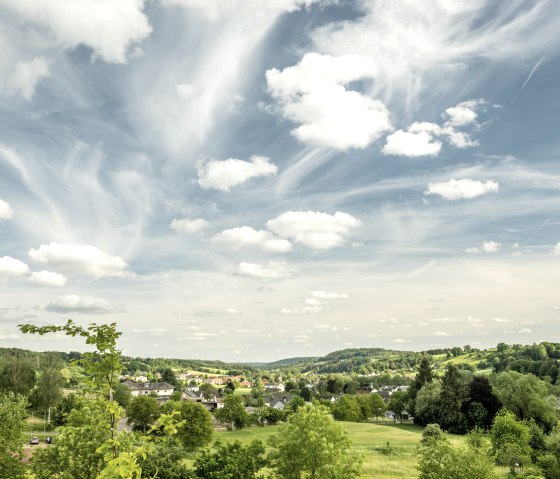 Paysage vert avec des champs, des arbres et un village. Le ciel est bleu avec des nuages blancs qui s'étendent sur la scène., © Eifel Tourismus, Dominik Ketz